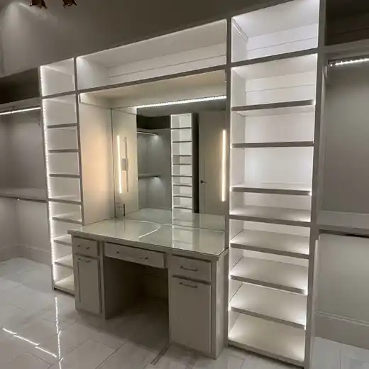 Custom walk-in closet with built-in shelving, under-shelf lighting, and a central vanity area with illuminated vertical light bars flanking the mirror.