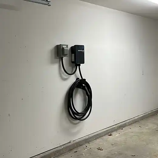 Electric vehicle (EV) charging station, with coiled black cable and plug, mounted on a white wall in a garage.