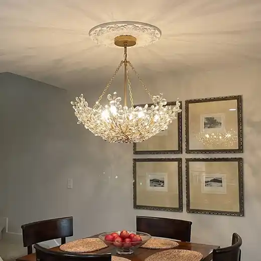 Elegant dining room featuring a gold and crystal chandelier with a decorative ceiling medallion, above a dark wood table with a fruit bowl, and four framed black and white pictures on the wall.